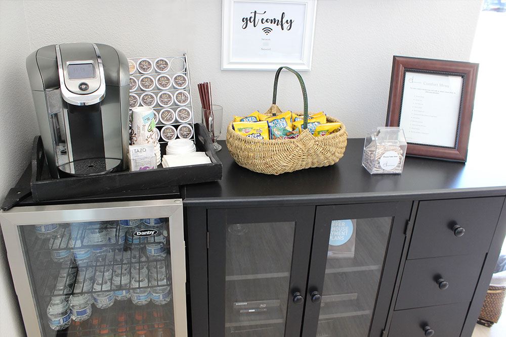 a desk with a coffee maker, a bag of snacks, and a framed picture on it
